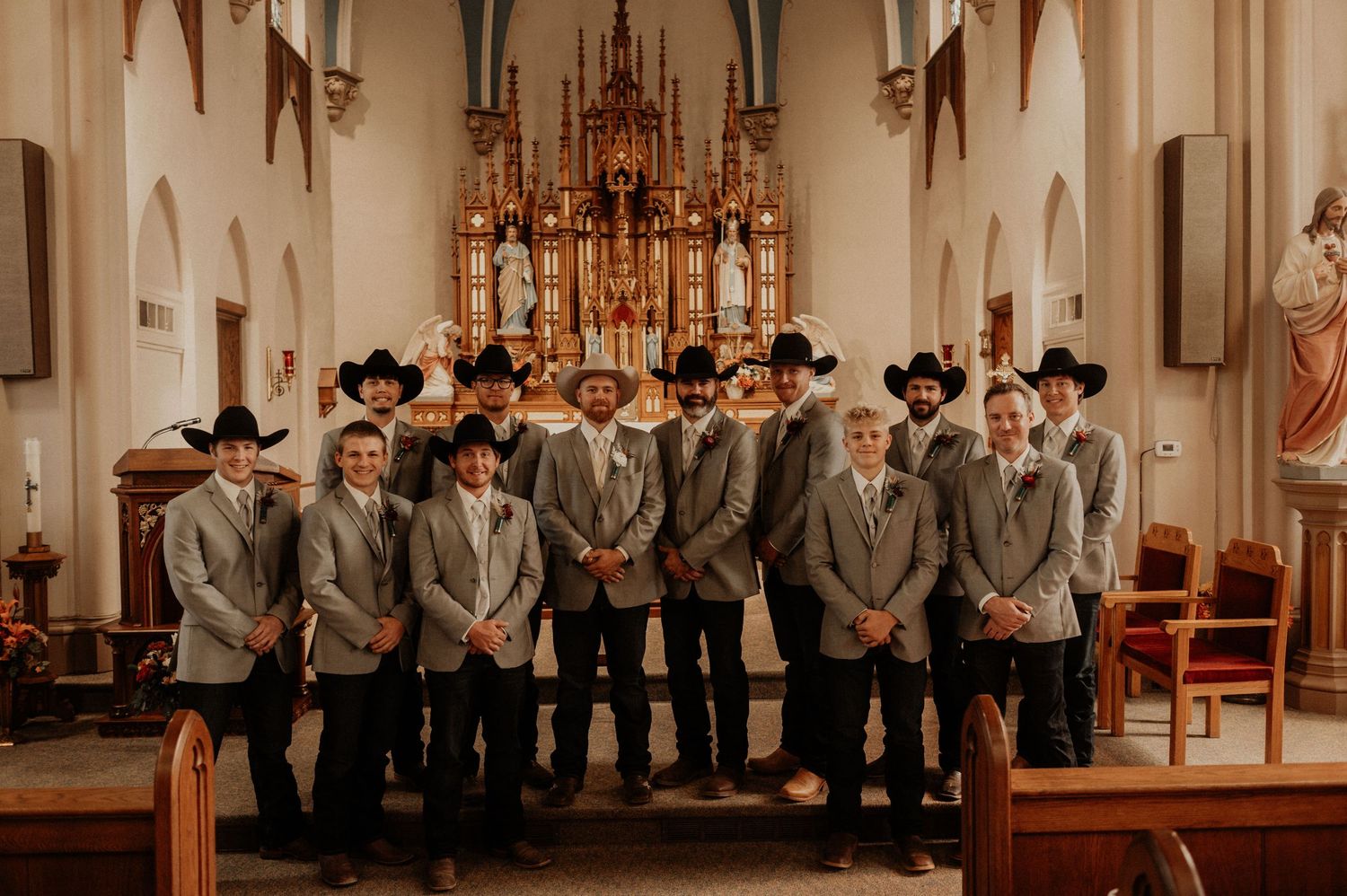 Wedding party members in gray suits stand in formation inside an ornate church.