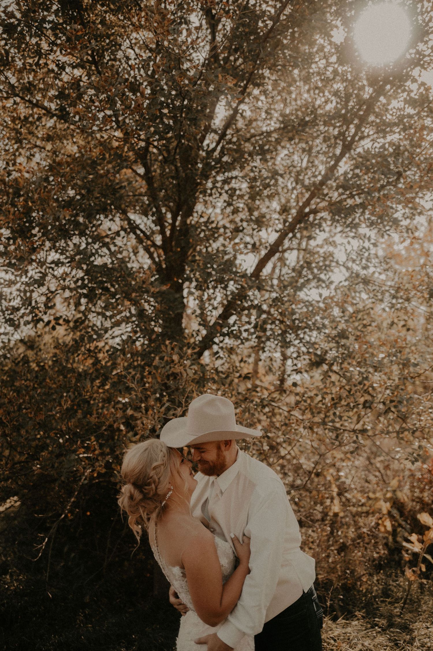 Newlyweds share an intimate moment under sunlit autumn foliage.