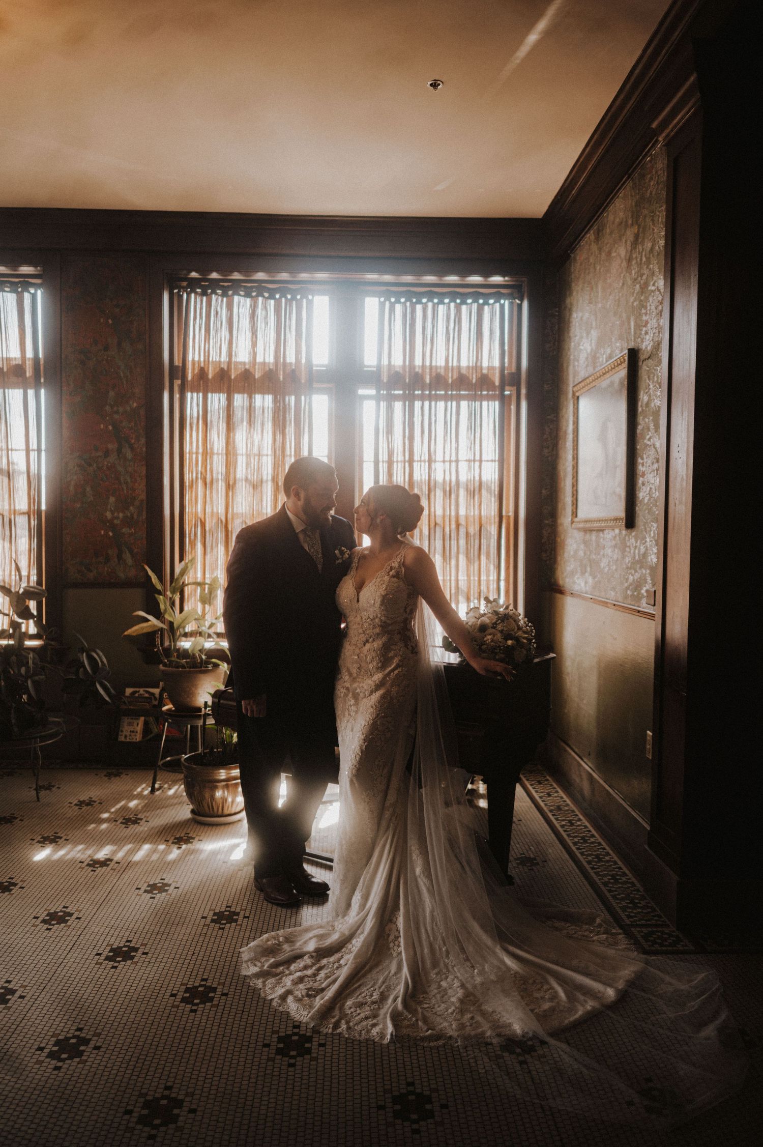 Atmospheric wedding photography in a dimly lit historic room with window backlighting.