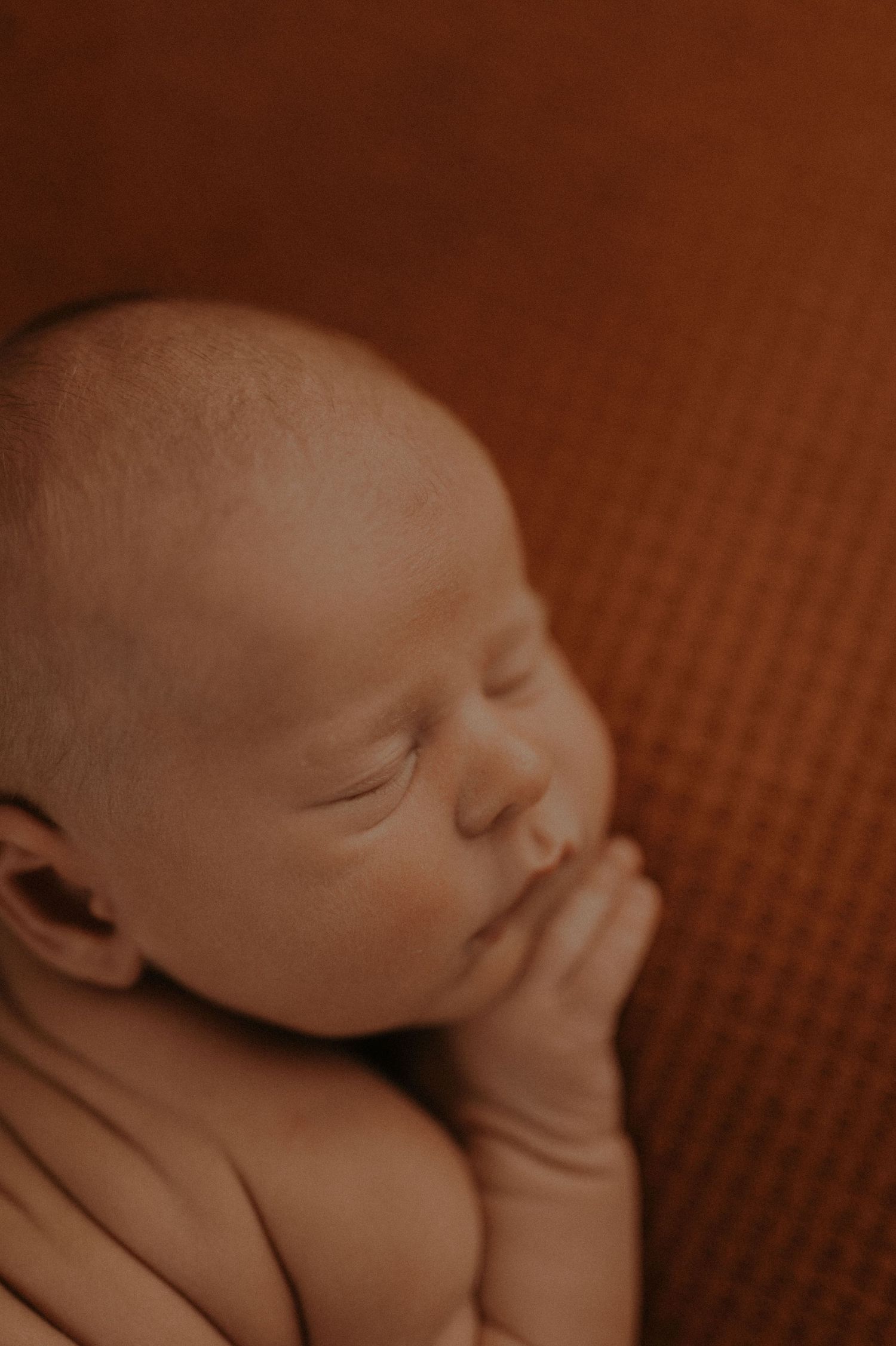 A sleeping newborn baby rests peacefully against a brown textured background in warm sepia tones.