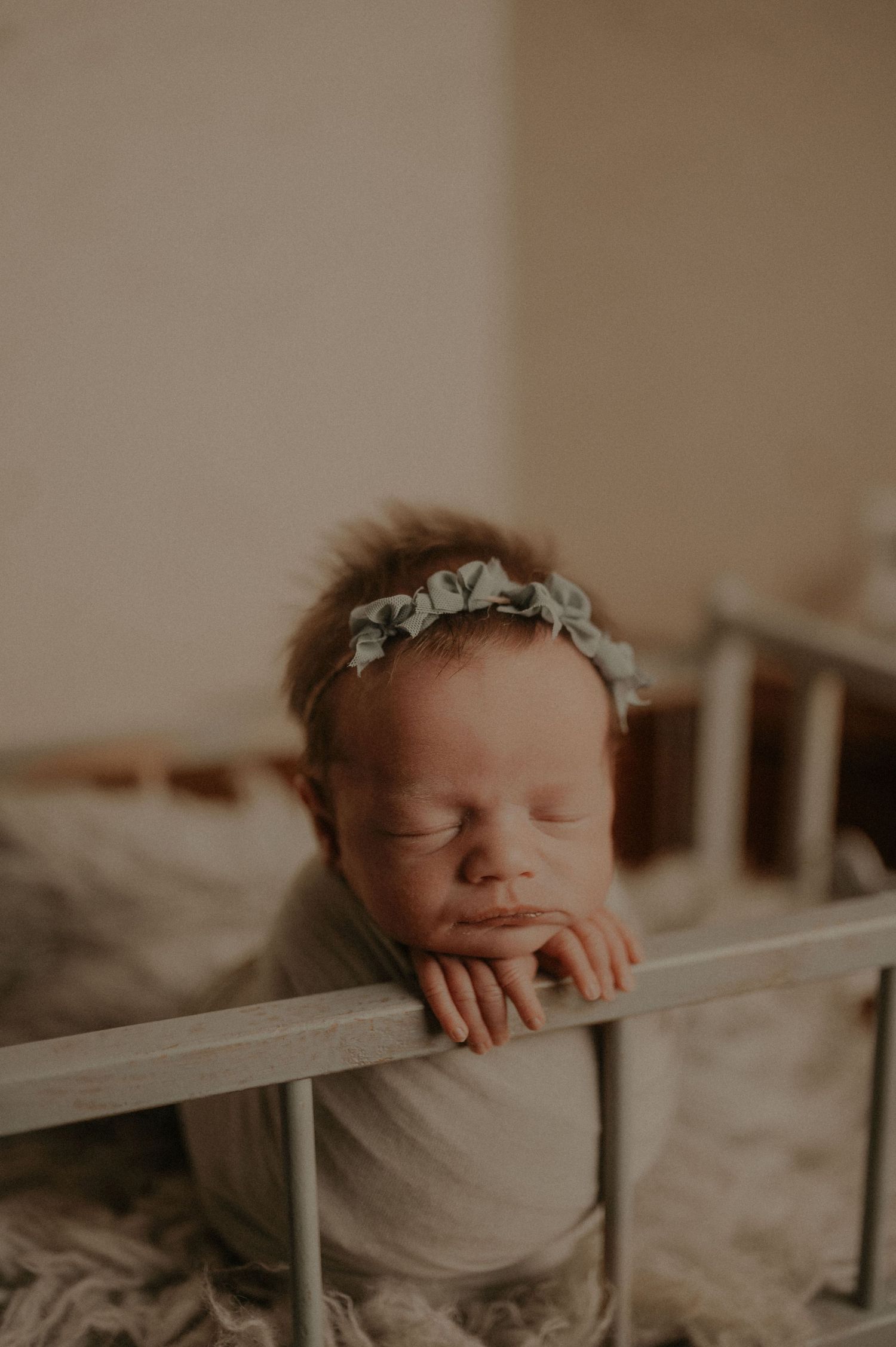 Gentle newborn portrait through white fence with soft natural lighting.