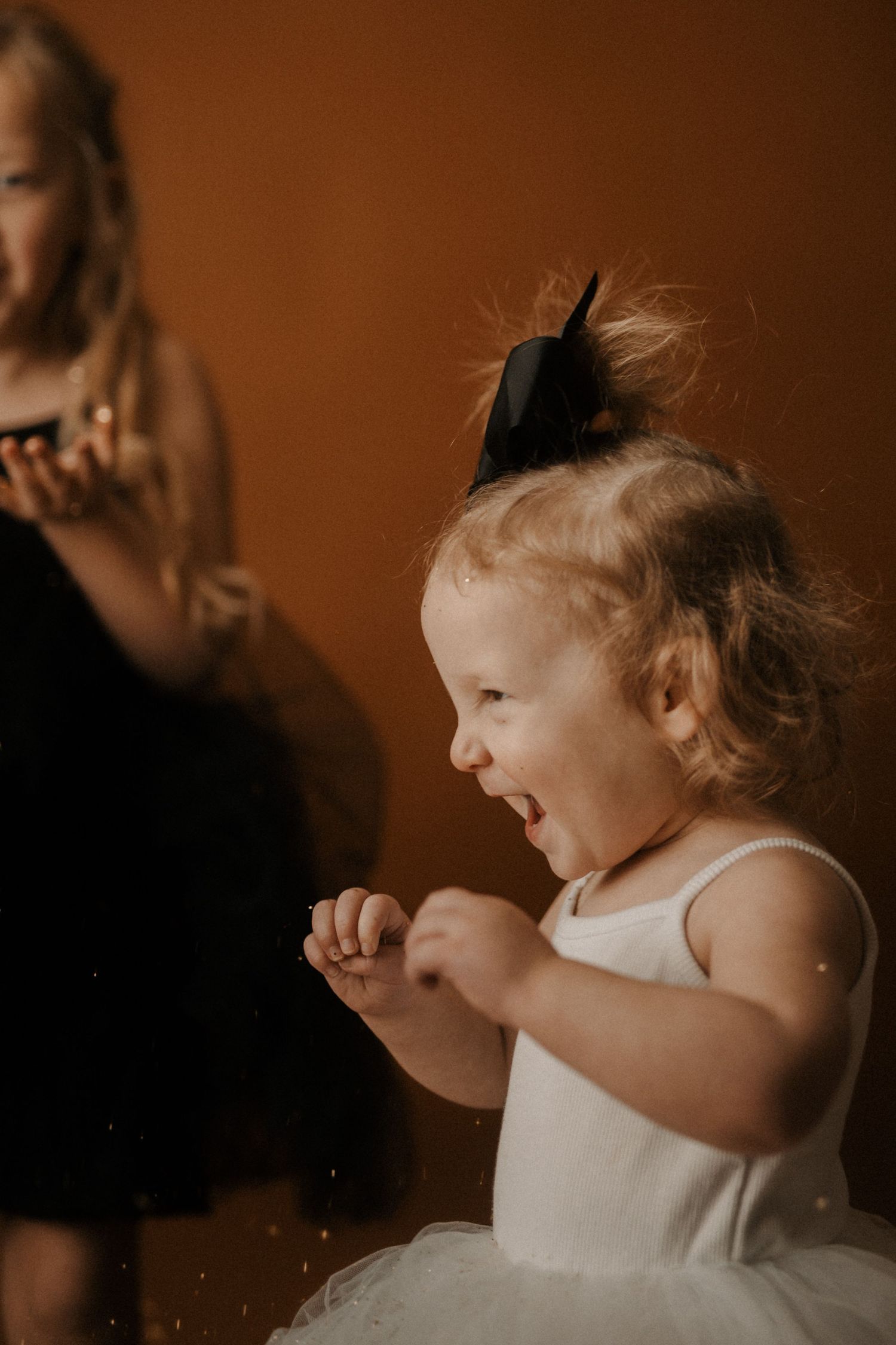 A child in a white dress smiles and laughs in a warm-toned setting with a sepia-like atmosphere.