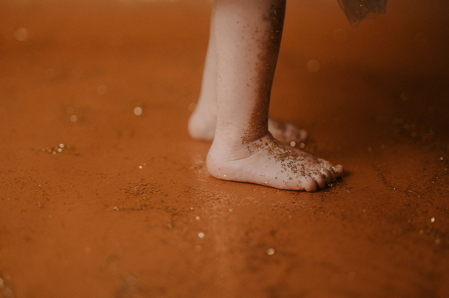 Bare feet standing on a rustic brown floor with sparkly glitter scattered around them.