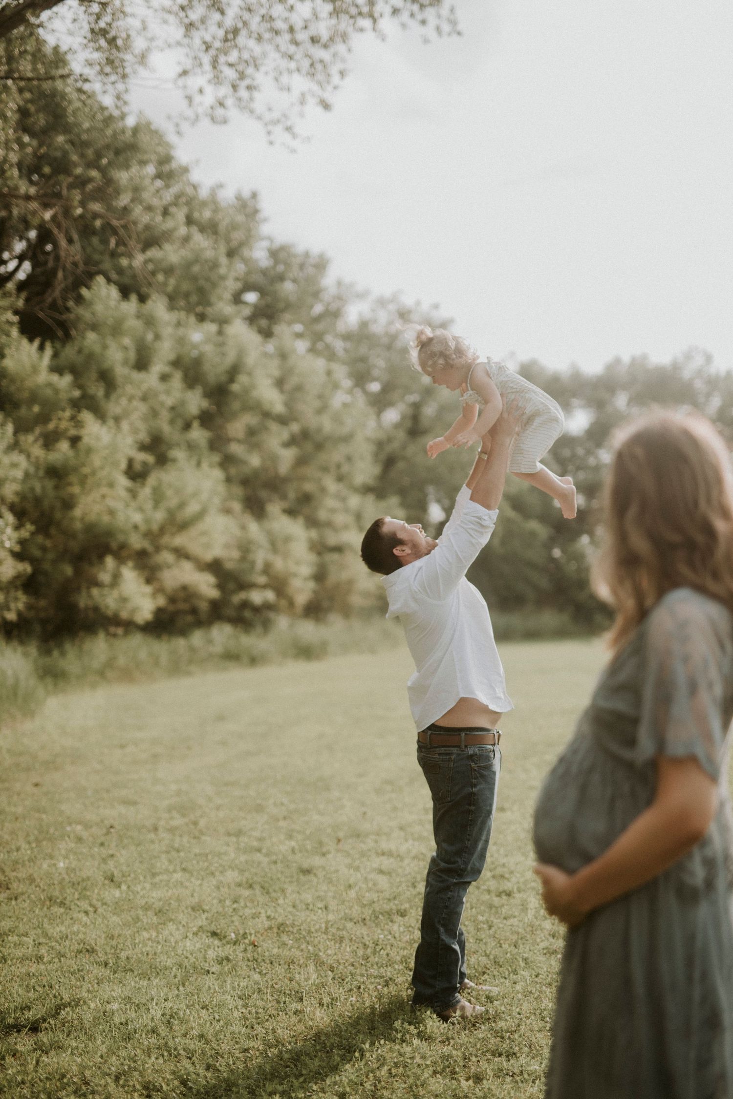 A couple plays together in a sunny field during a warm summer evening, creating a joyful and candid moment.