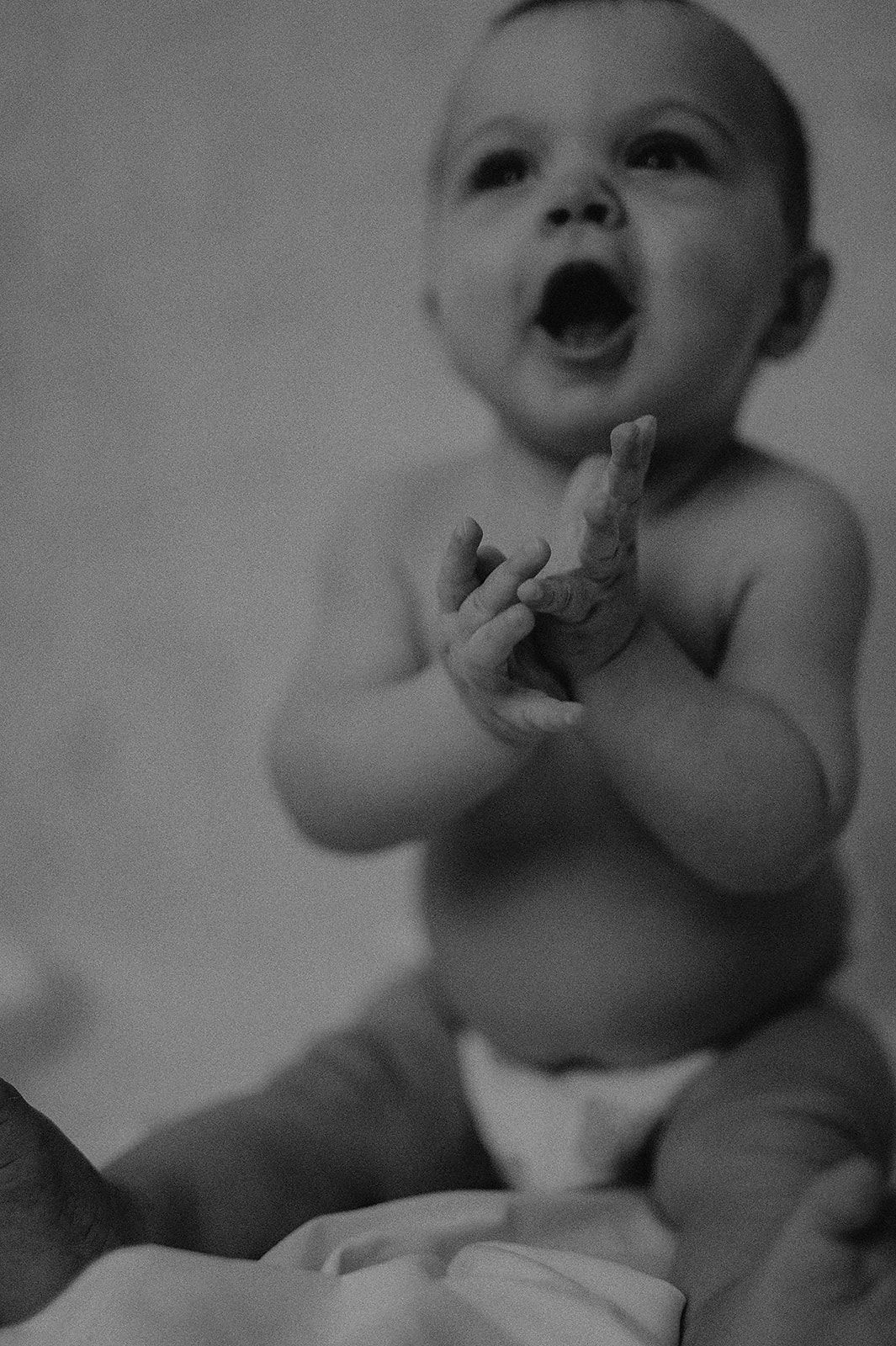 Black and white photo of an excited baby in a diaper gesturing with their hands.