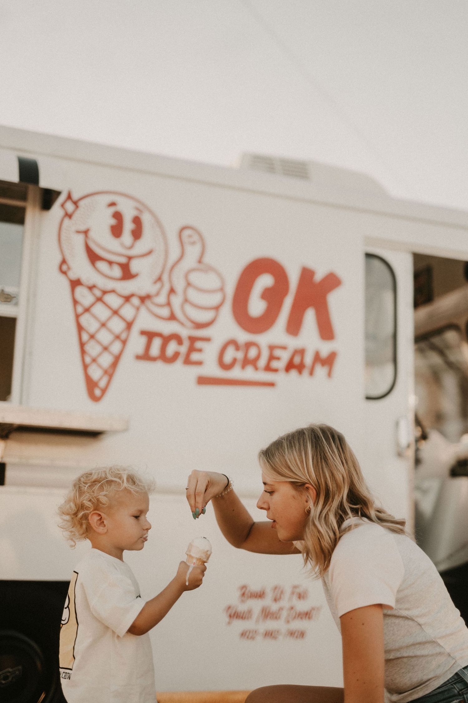Mother and child sharing ice cream moment in front of shop wall with ice cream graphics.