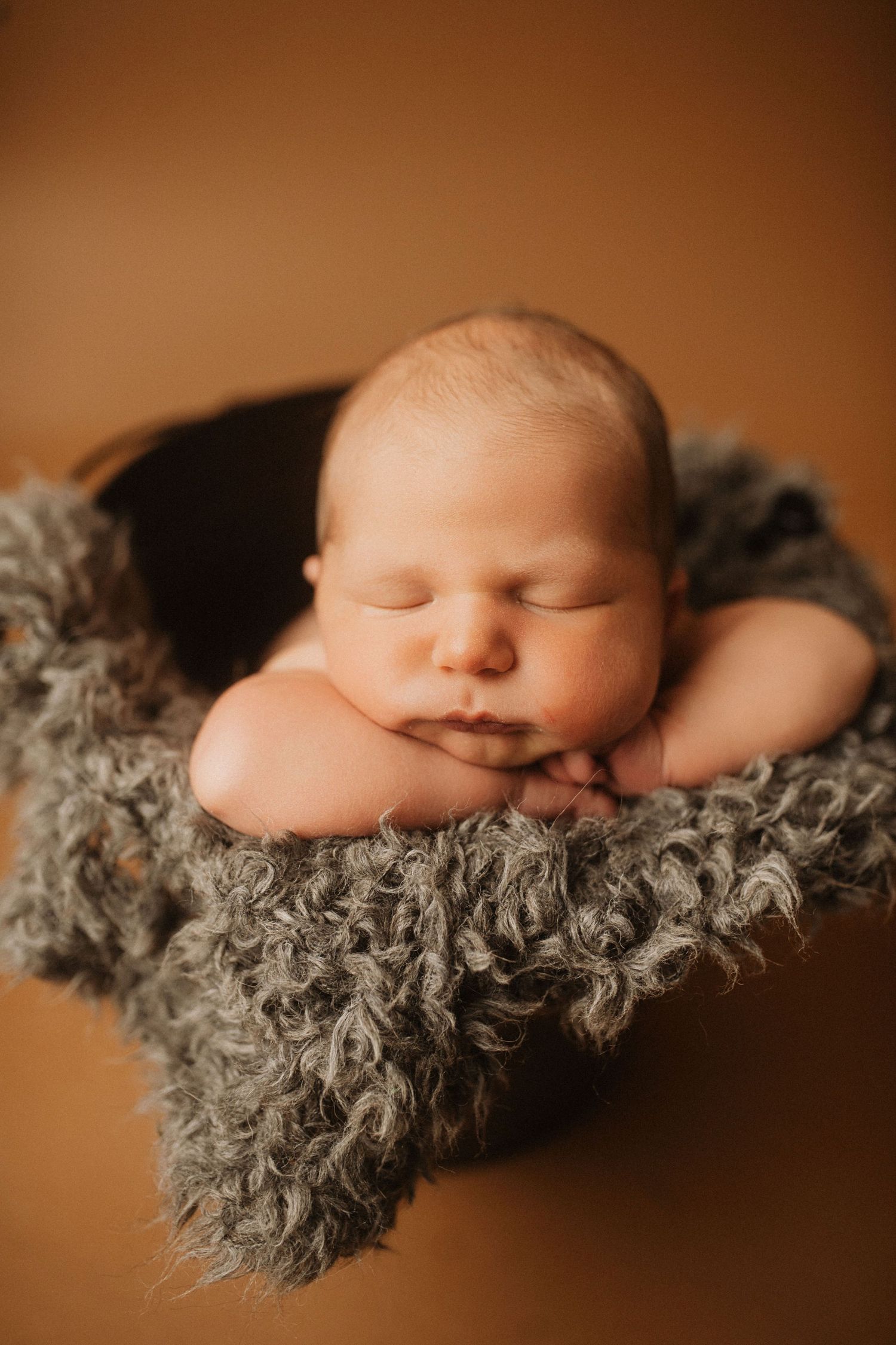 Peaceful newborn sleeping on gray fluffy blanket against warm brown background.