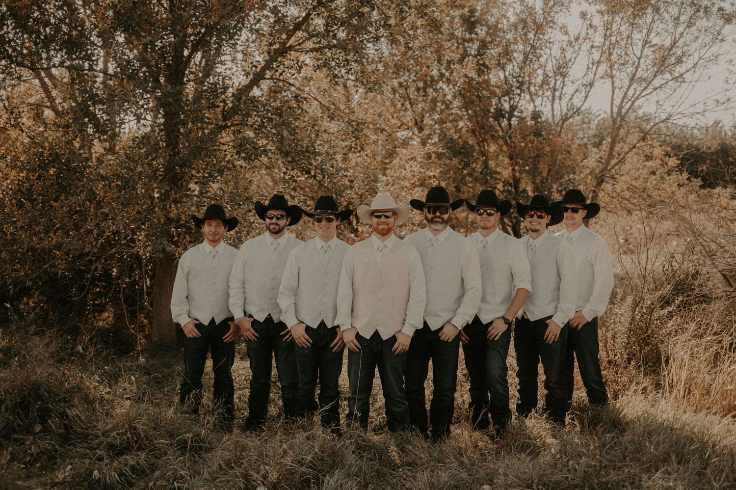 Wedding party members lined up outdoors against autumn foliage backdrop.