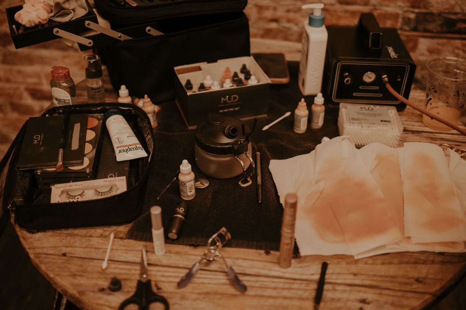 Makeup supplies and tools arranged on a wooden surface in vintage lighting.