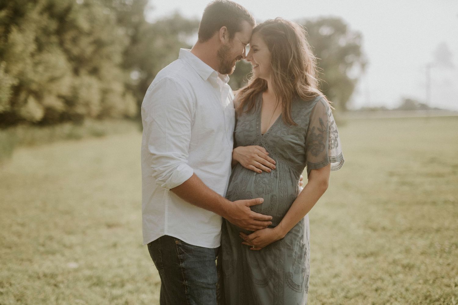A couple embraces in a sunlit grassy field during a romantic outdoor photoshoot.