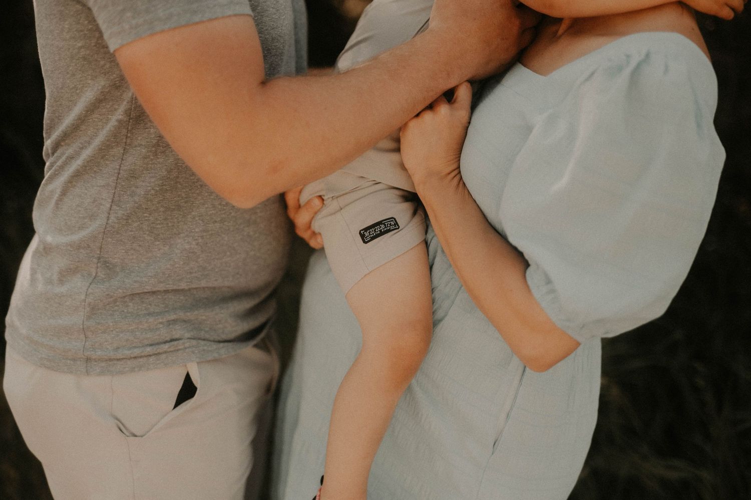 Close-up view of a parent holding a sleeping baby wearing white clothes against a dark background.