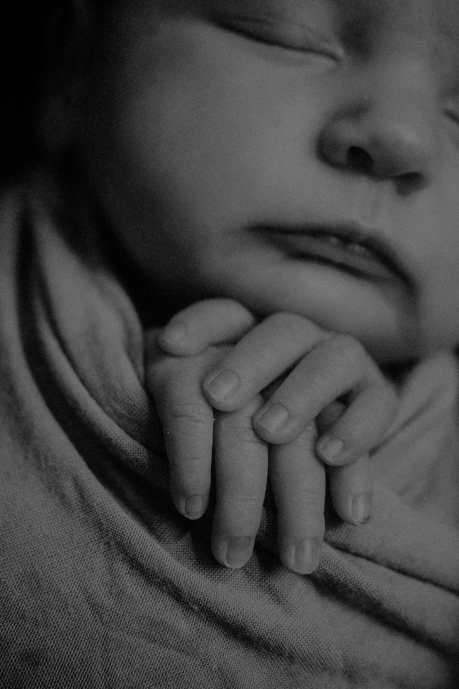 A black and white close-up photo shows a baby's tiny hand resting gently against someone's face.