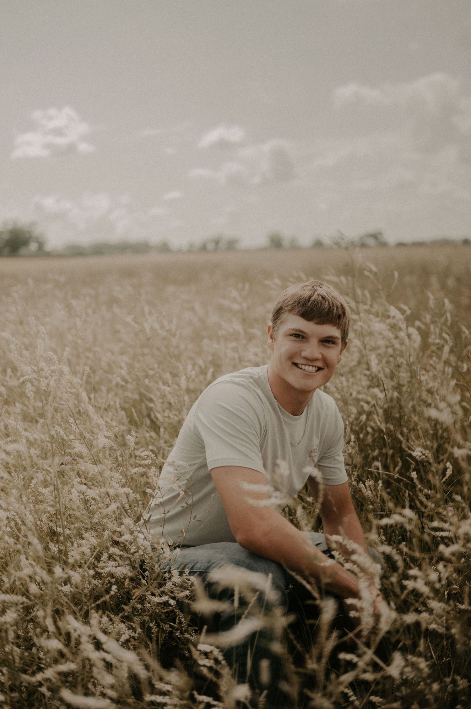 A person sits and smiles in a golden field during sunset, creating a warm and dreamy outdoor portrait.