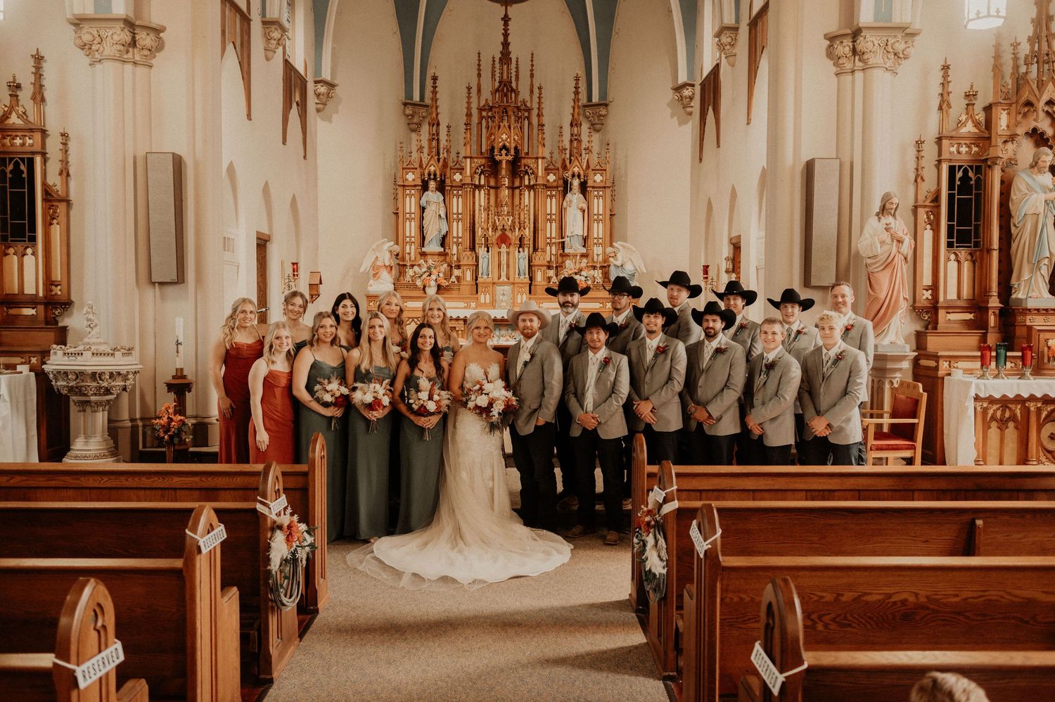Wedding party stands in a beautiful Catholic church with ornate golden altar and vaulted ceilings.