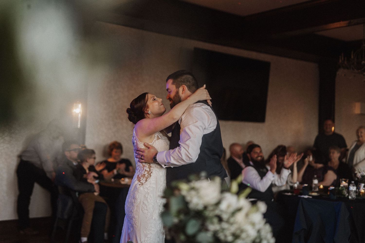 Wedding couple dances together in a dimly lit reception hall.