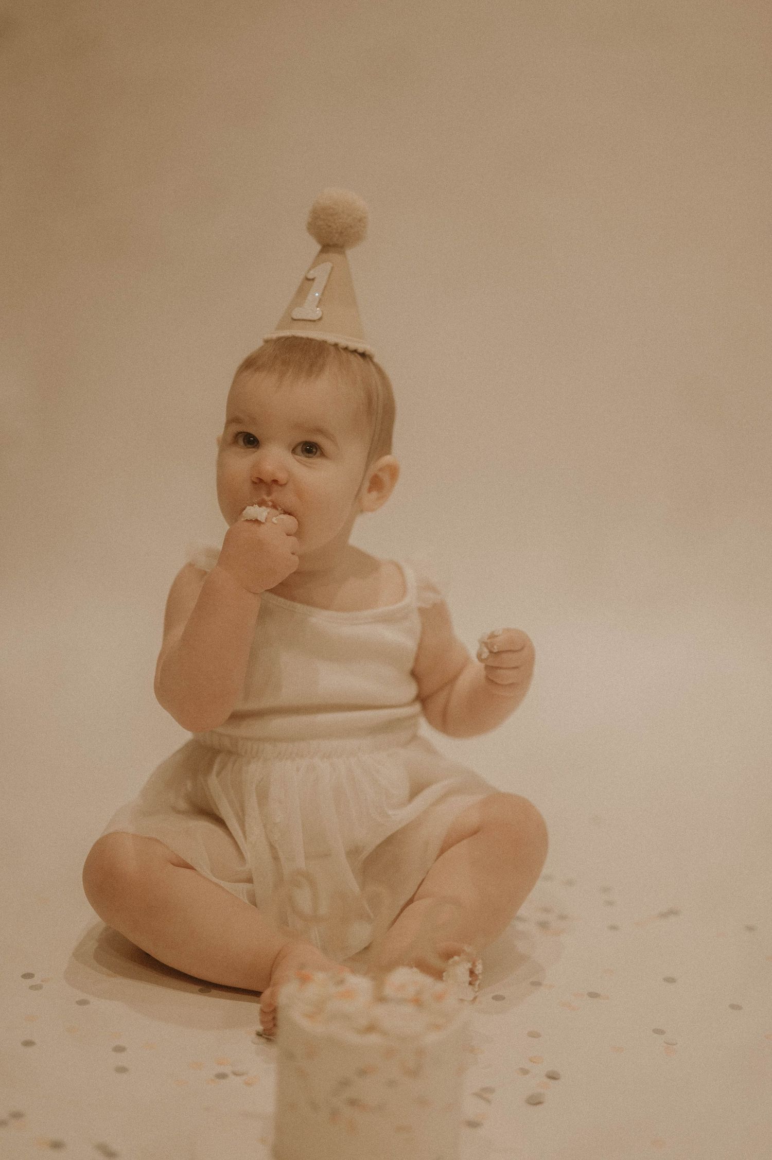 A baby in white clothing sits on a polka dot surface in a sequence of four similar poses.