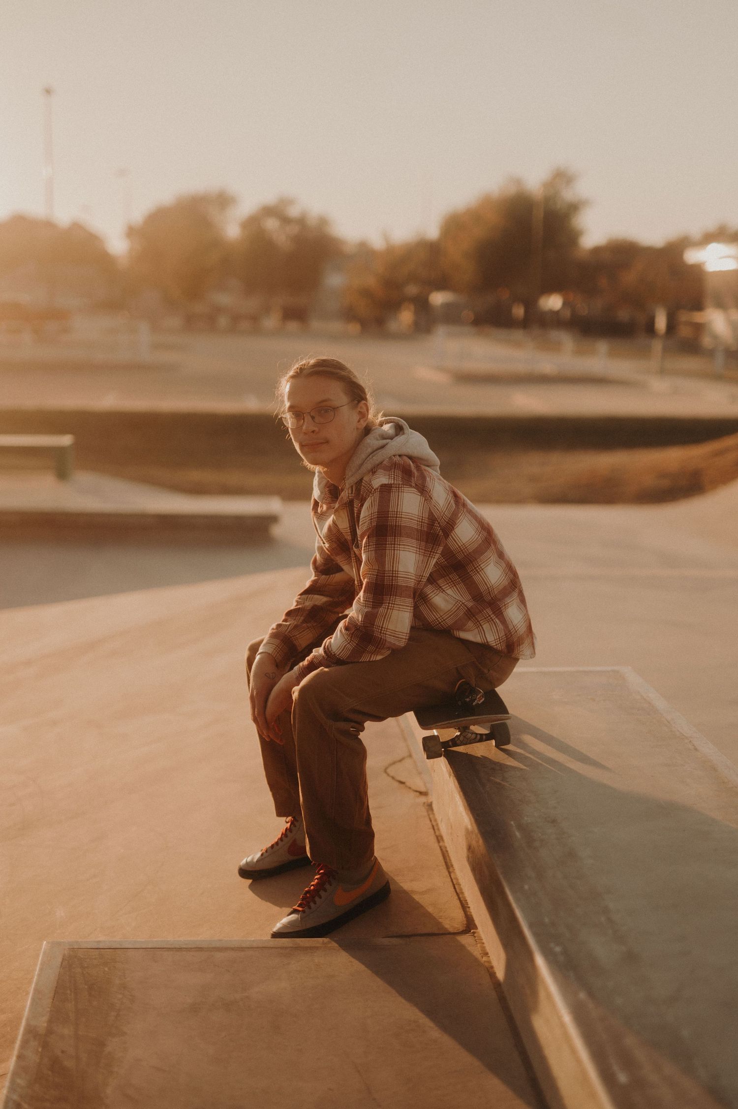 Young skateboarder sits on a concrete ledge during golden hour in an urban setting.