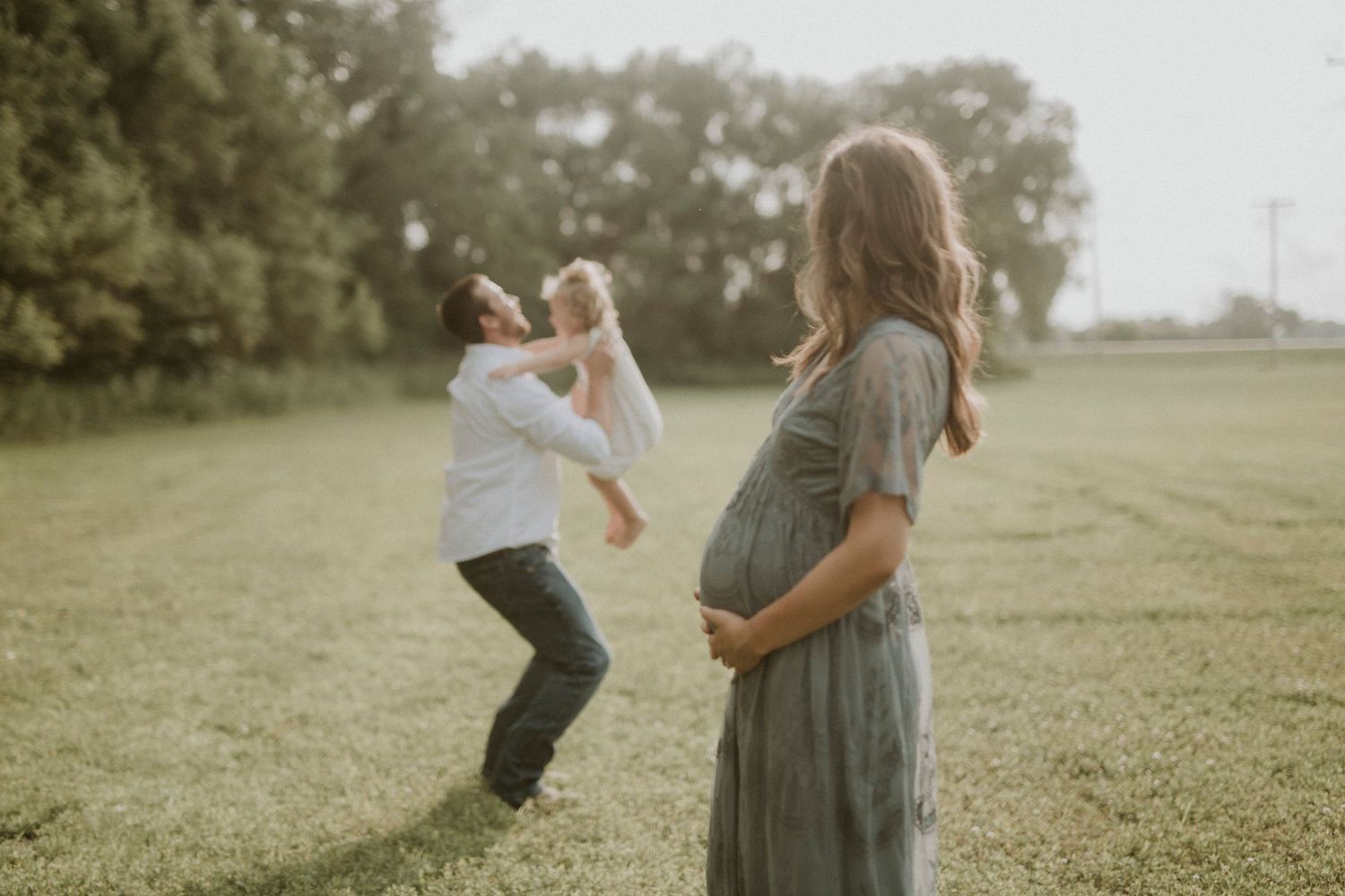 A family plays together and chases each other in a grassy field on a sunny afternoon.
