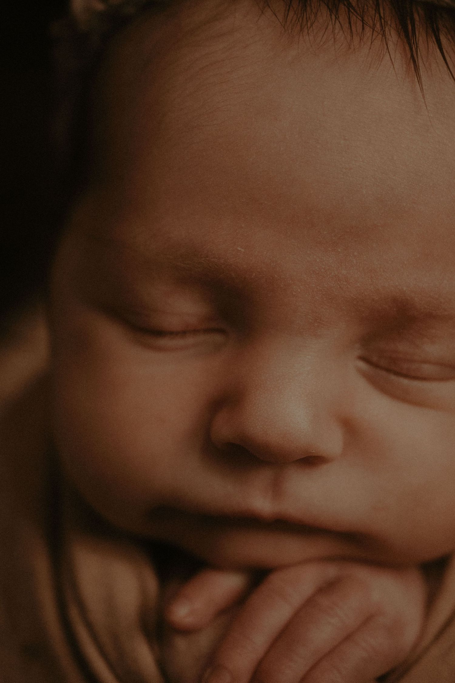 A series of sepia-toned close-up photos showing a baby's expressions changing from sleeping to smiling.