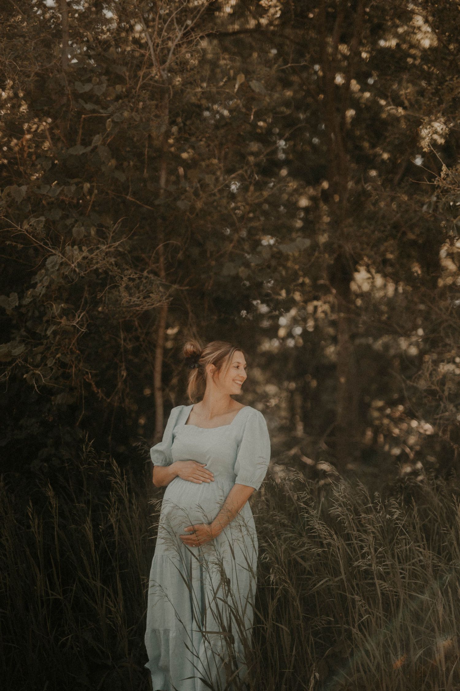 A maternity portrait in a dreamy outdoor setting with soft lighting and tall grass.