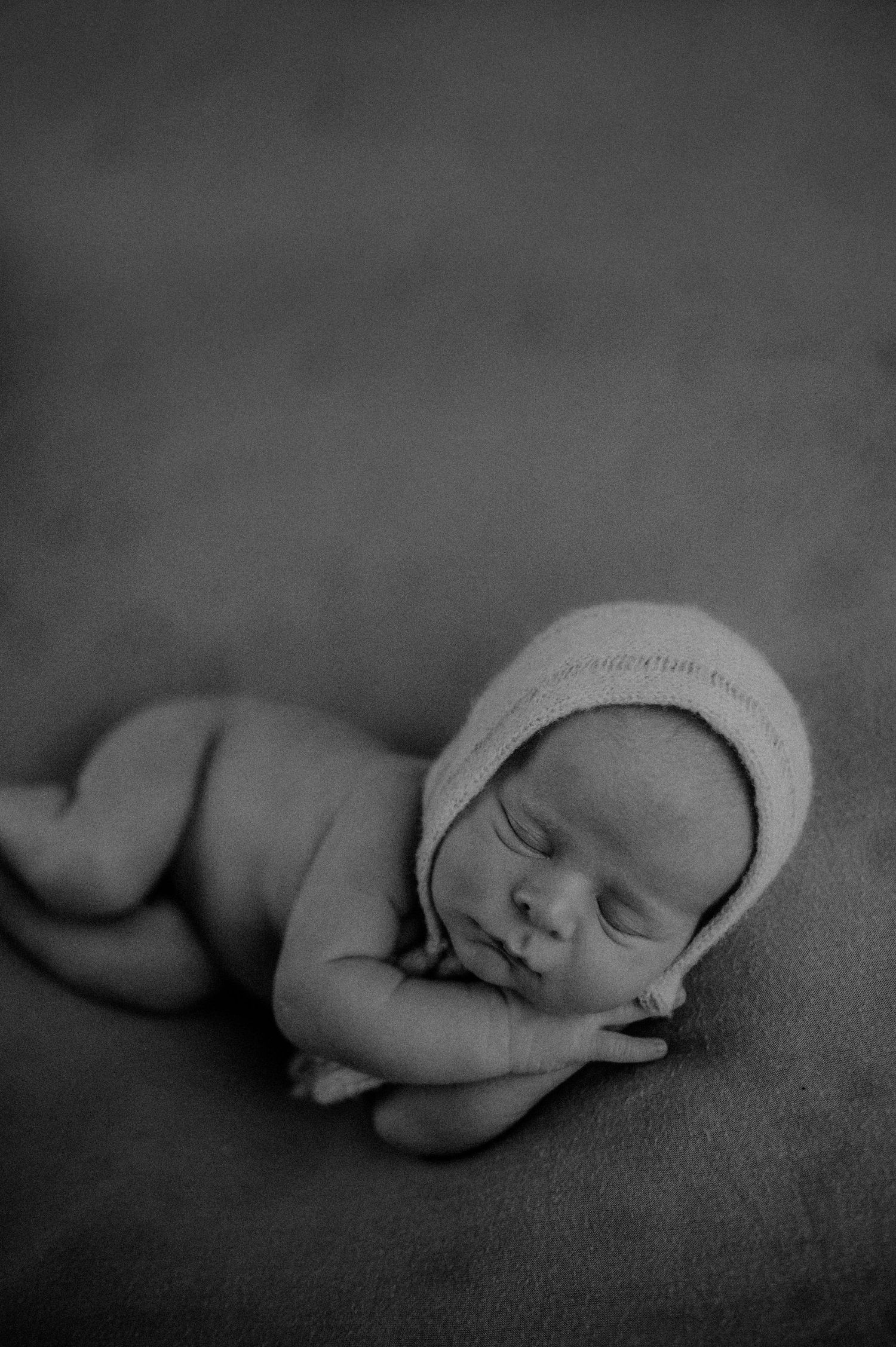 Sleeping newborn wearing knit cap in artistic black and white portrait.