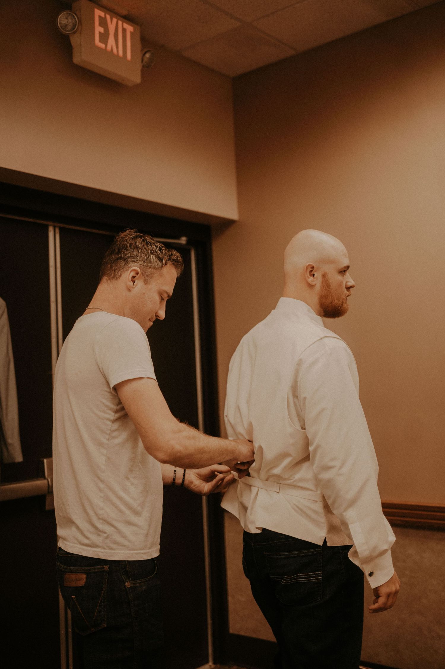 People in white shirts interacting in a dimly lit room near an exit sign.