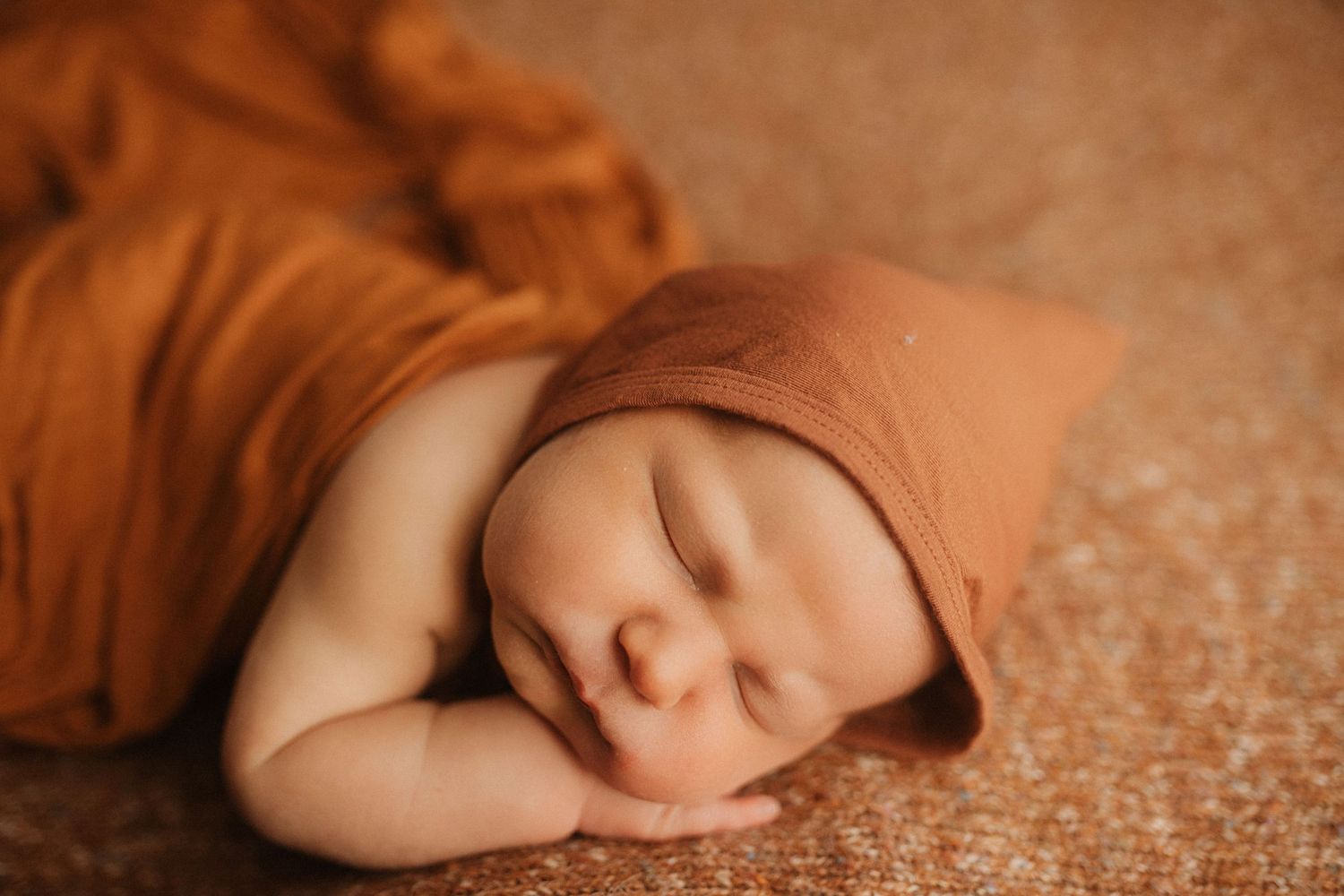 Sweet sleeping newborn posed on warm brown textured backdrop.