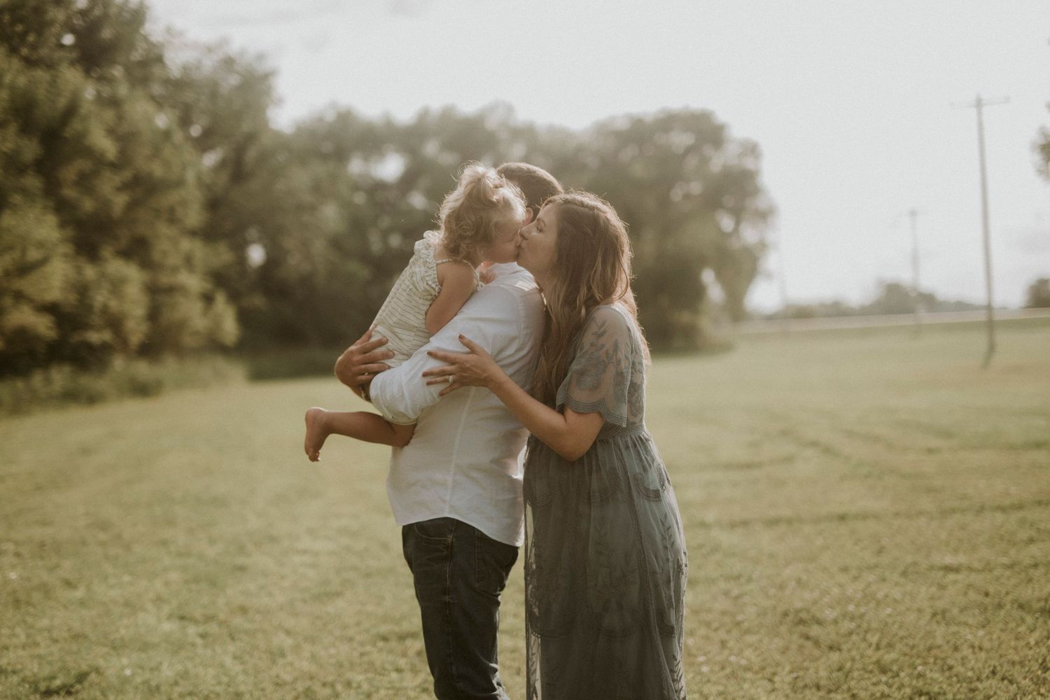A couple shares an intimate moment together in a sunlit grassy field during golden hour.