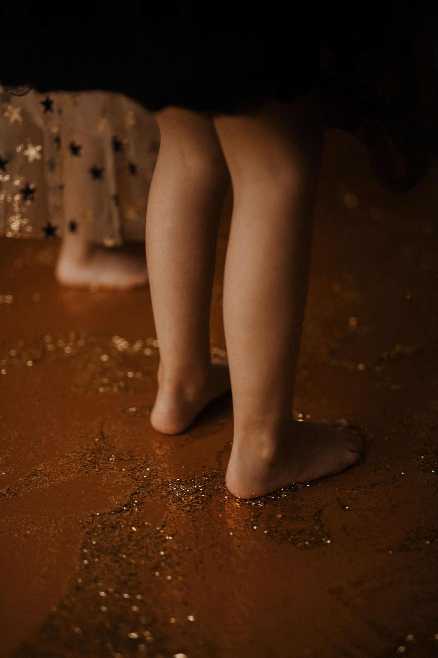 Bare feet walking on a dark brown surface with scattered white specks or glitter creating a dreamy atmosphere.