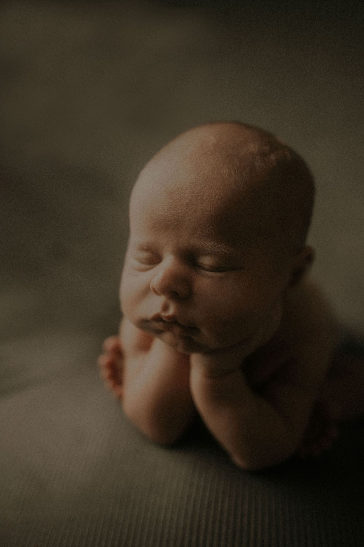A series of peaceful newborn sleeping portraits in warm, moody lighting on textured fabric.
