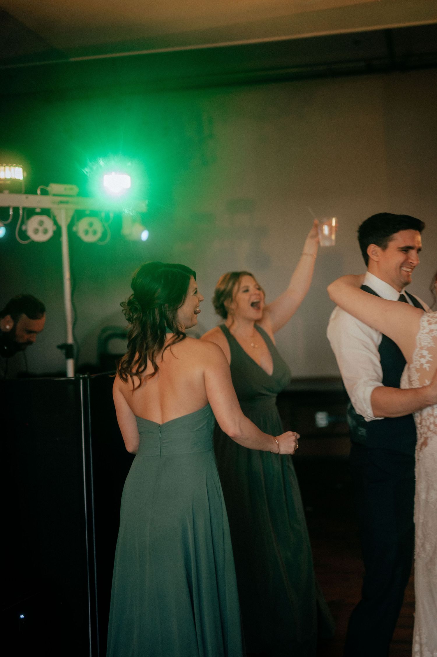 Wedding guests dancing energetically on a dimly lit dance floor with green lighting effects.