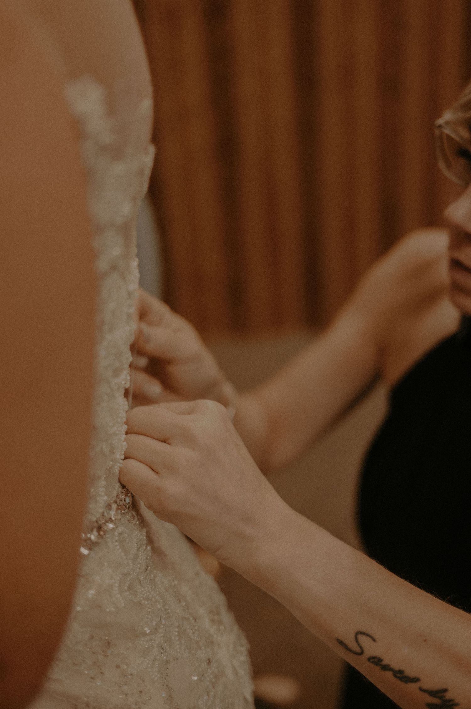 Hands adjusting the back buttons of a detailed lace wedding gown.