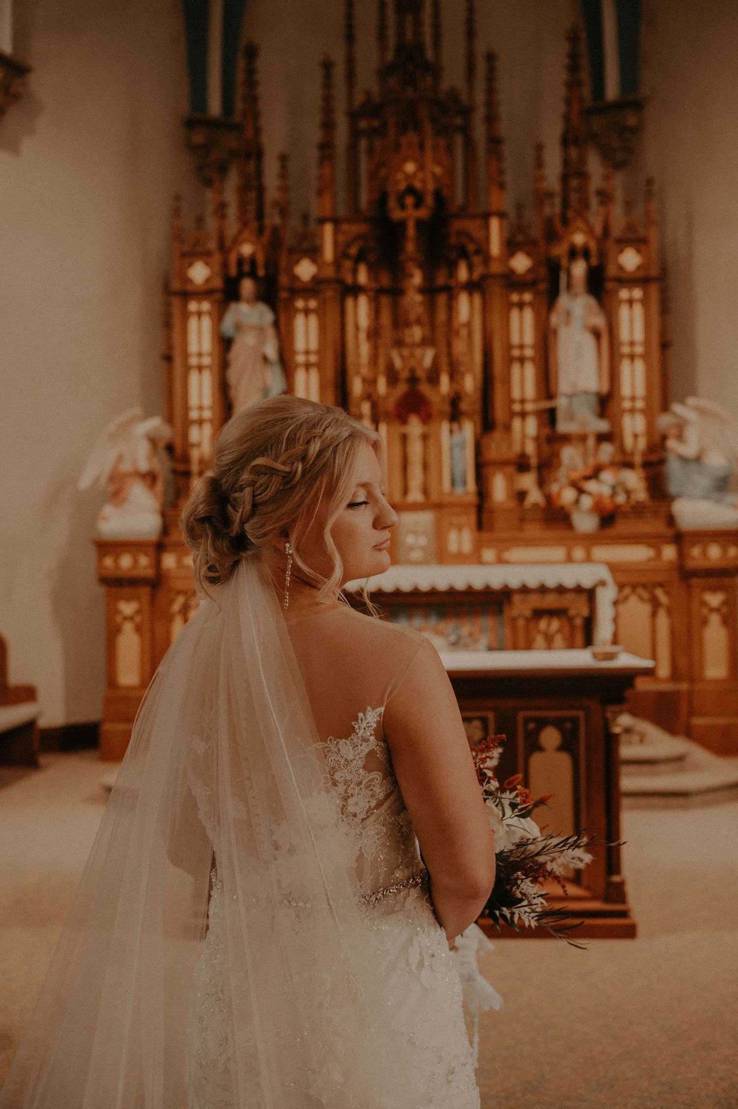Long white wedding veil trails behind bride in lace dress inside historic church.