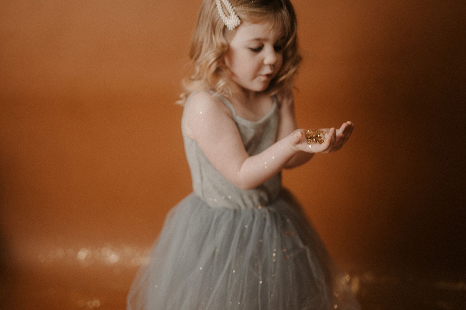 A young child in a gray dress twirls and dances against a warm brown backdrop.