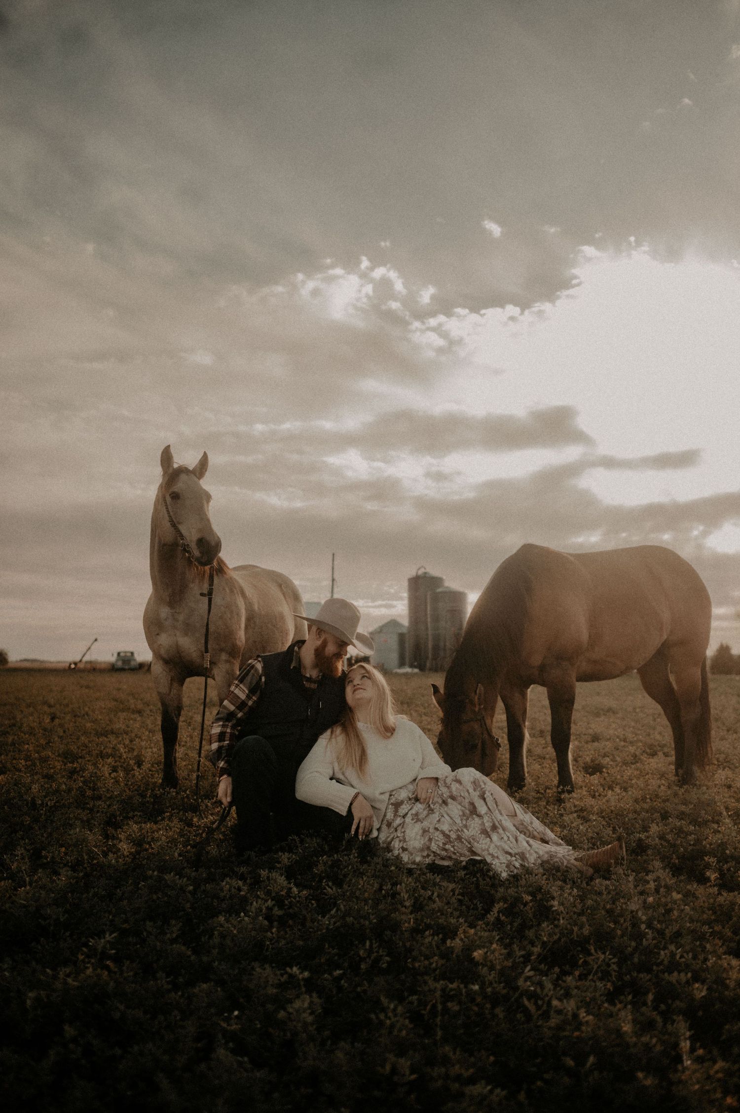 A romantic countryside photoshoot with horses against a dramatic cloudy sky and city skyline in the background.