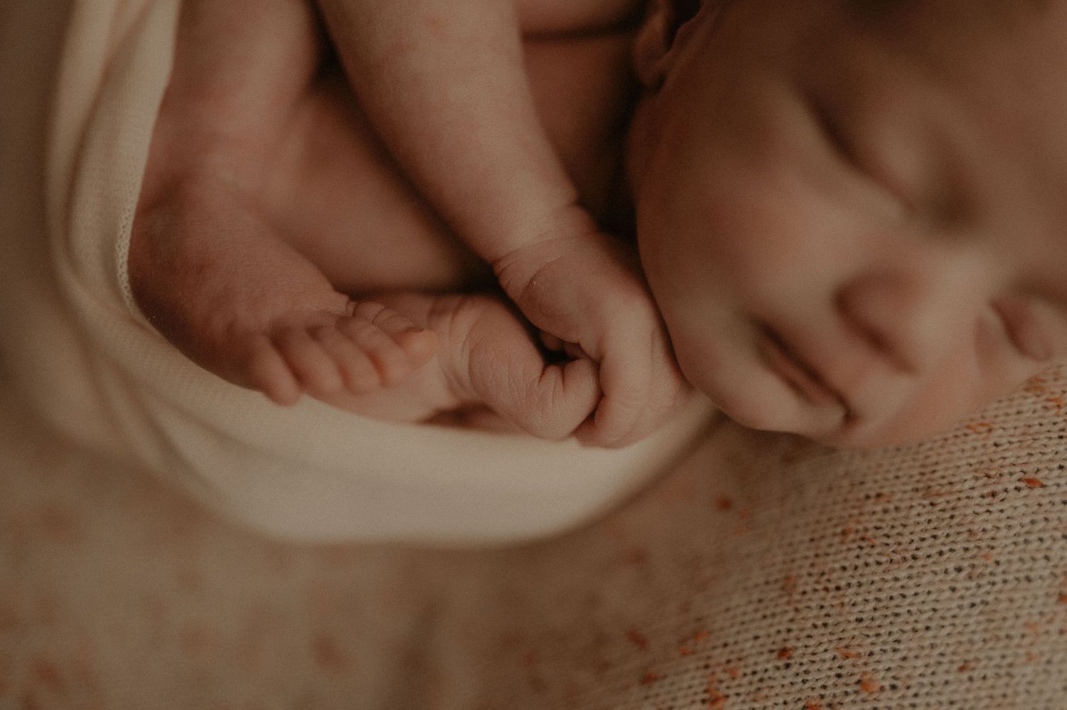 Close-up details of sleeping newborn on textured fabric in natural light.