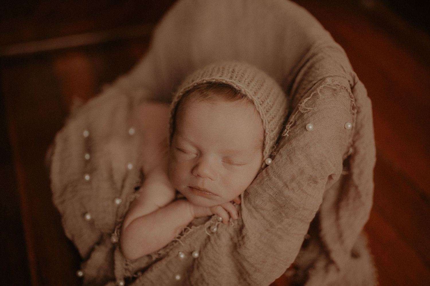 Artistic sepia newborn photography with delicate wrapping and soft shadows.