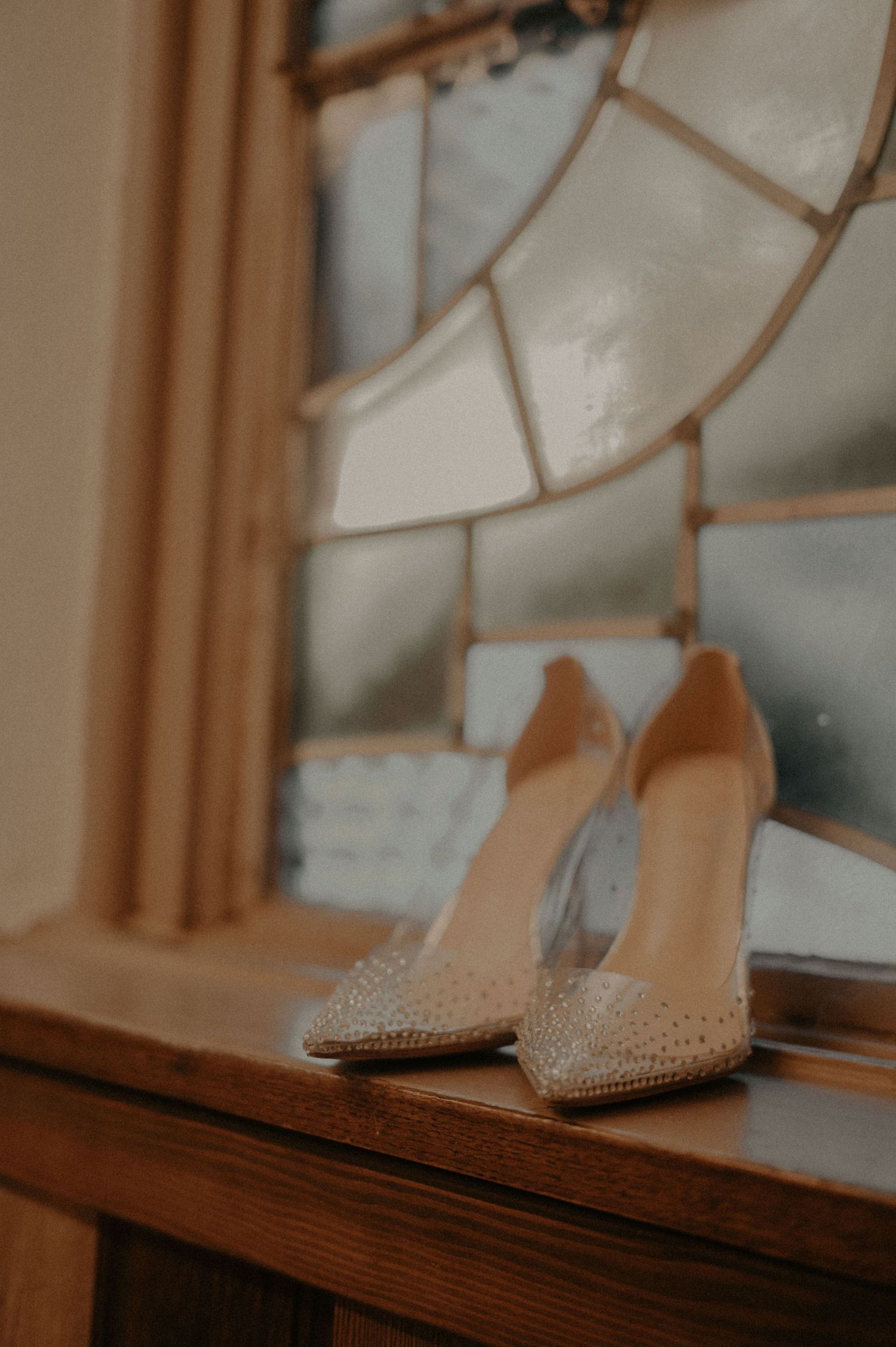 Elegant beige studded high heel shoes displayed on a wooden windowsill in warm lighting.