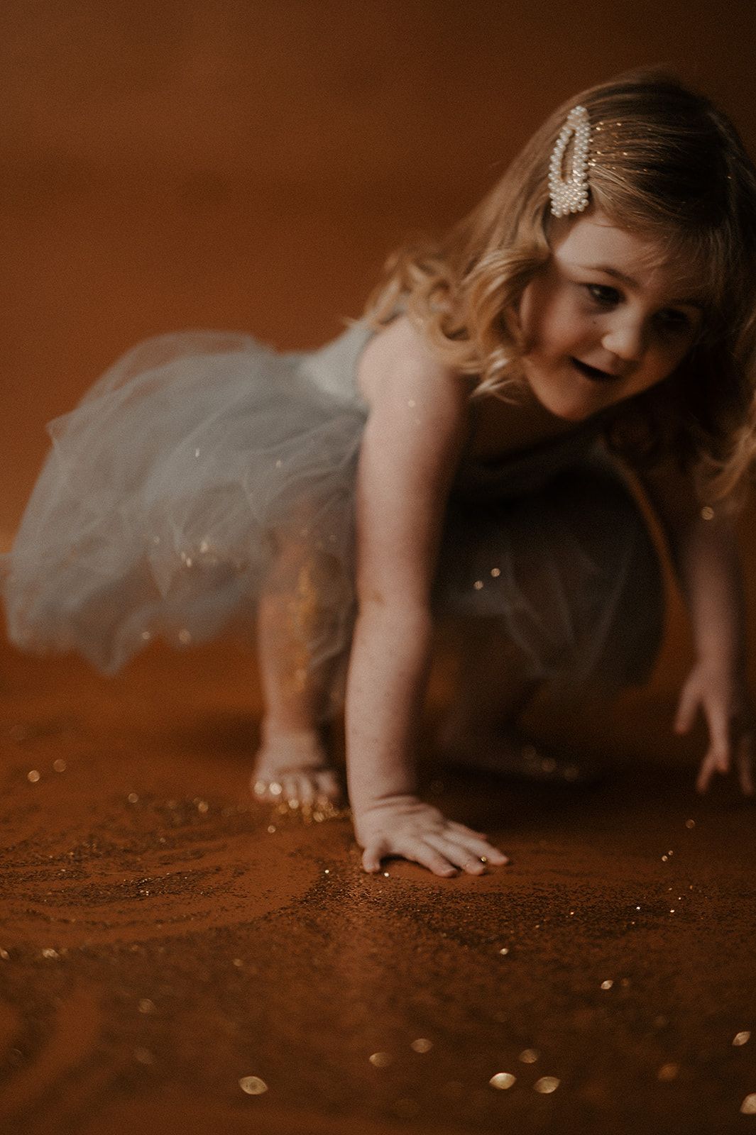 A young dancer in a white tulle dress crawls gracefully on a brown floor with a dreamy, moody atmosphere.