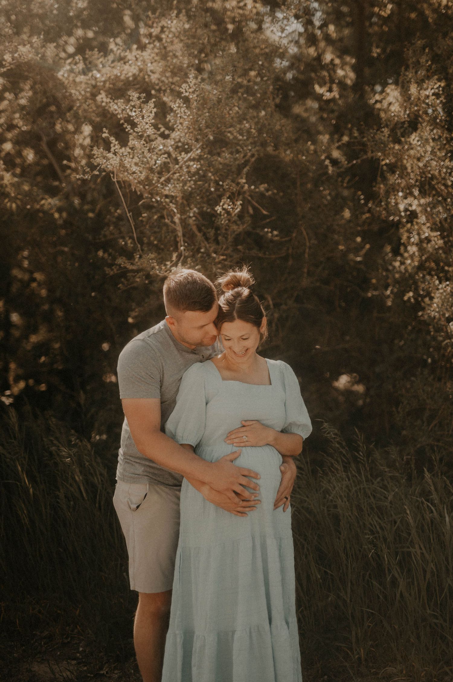 A couple shares an intimate moment in a field during sunset while expecting a baby.