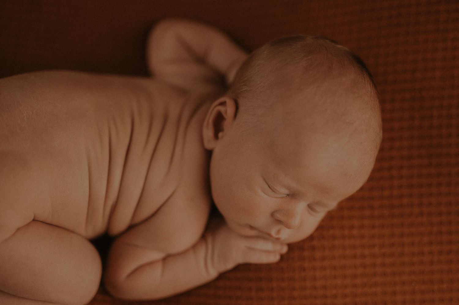 Peaceful sleeping newborn baby in warm sepia tones lying on textured fabric.