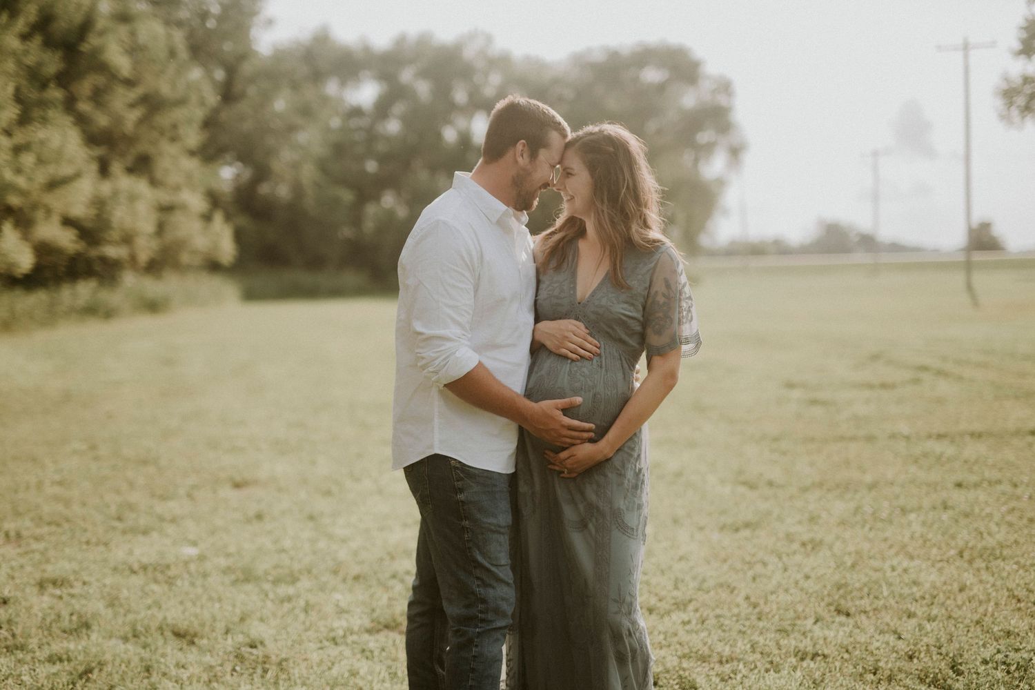 Couple embraces in a sunlit grassy field during golden hour photo session.