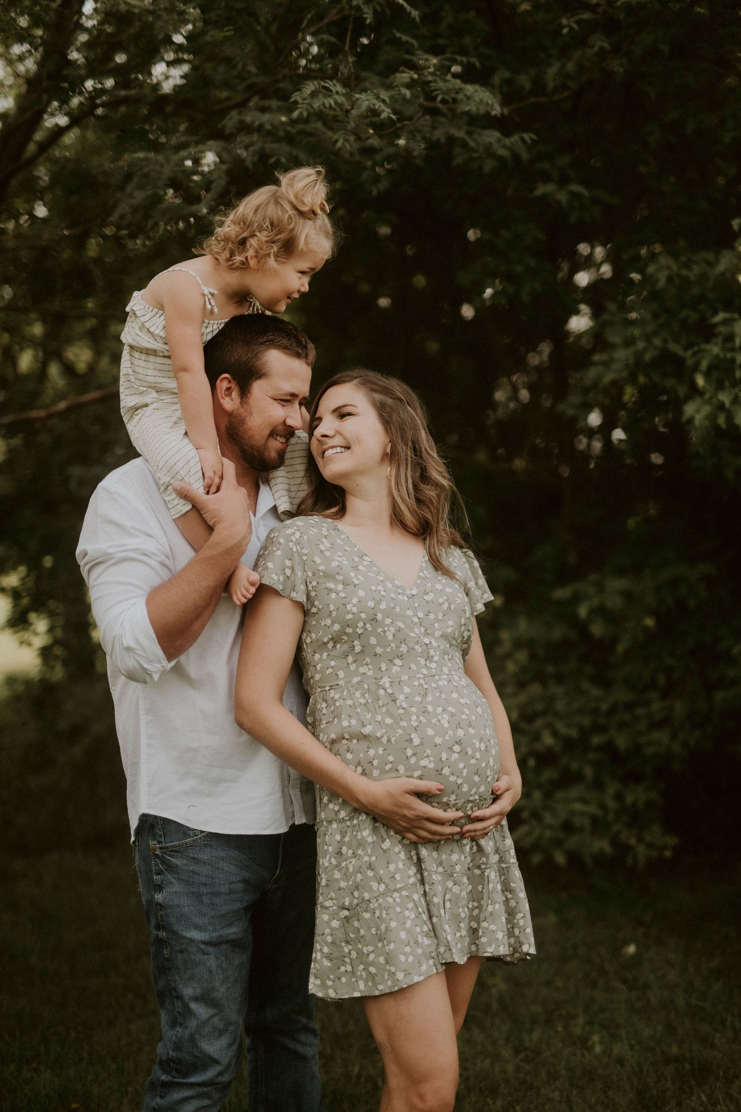 A couple shares intimate moments in a natural outdoor setting during a maternity photoshoot at sunset.