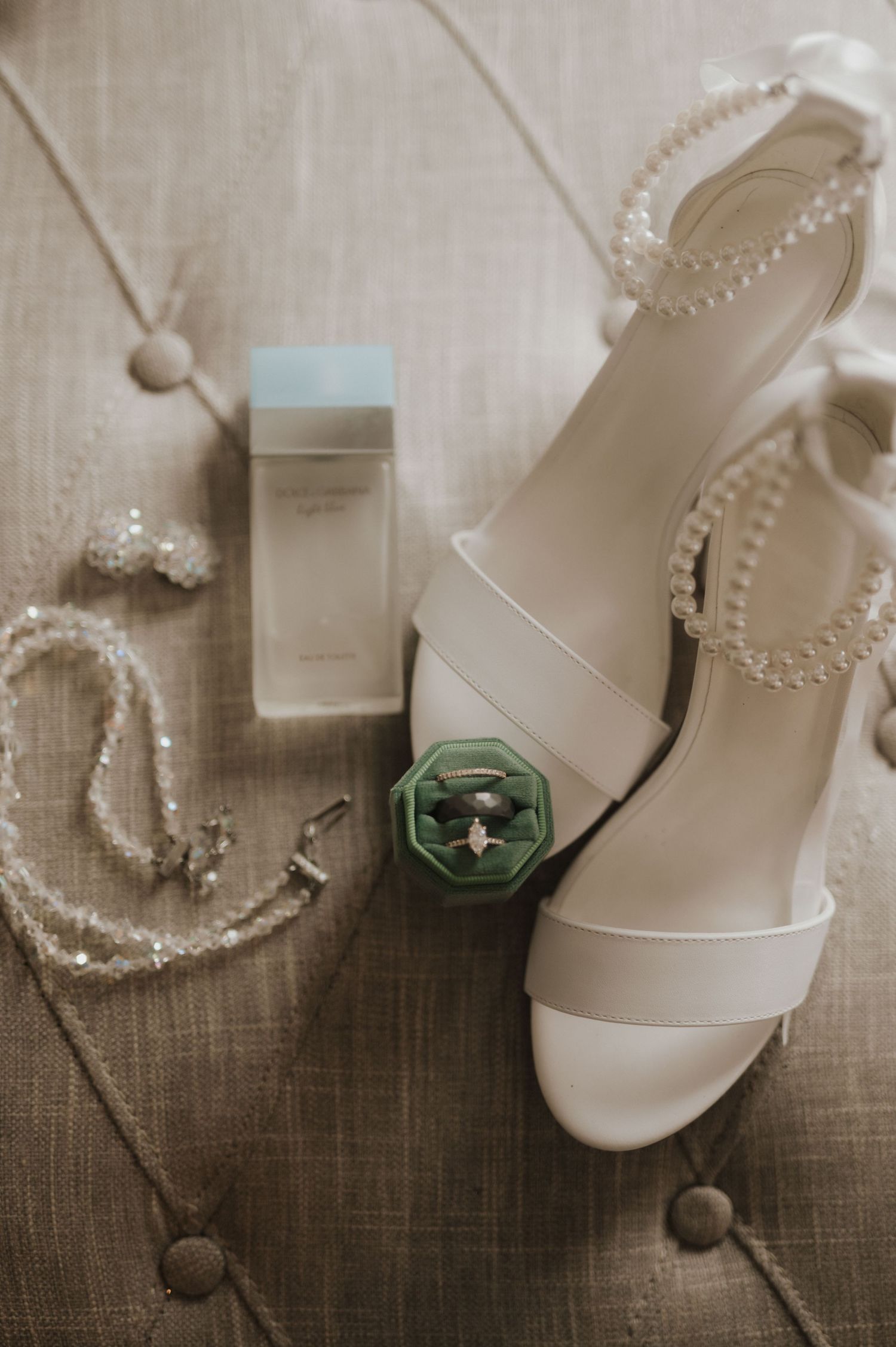 Wedding accessories including white shoes, pearl necklace, and green ring box on linen background.