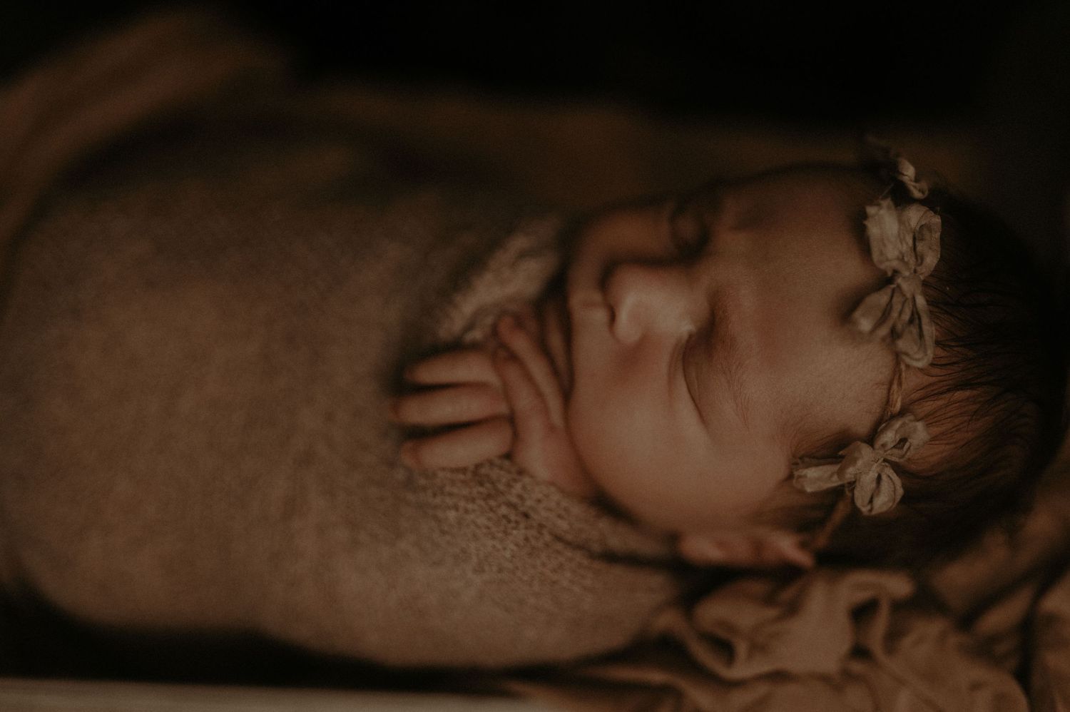 A sleeping baby wearing a delicate floral headband in a warm, sepia-toned close-up portrait.