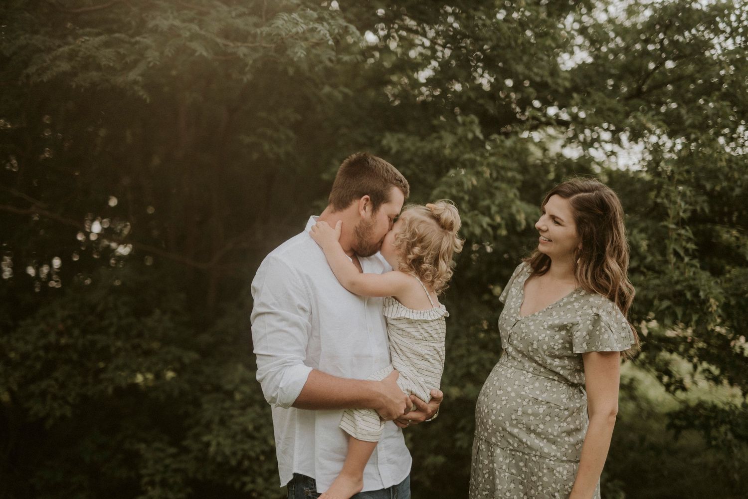 A couple embraces outdoors in a romantic photoshoot surrounded by lush greenery and natural light.
