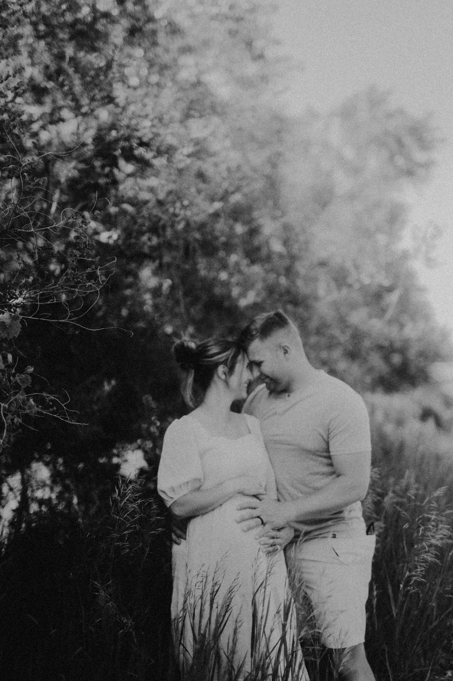 A romantic couple embraces in a dreamy outdoor setting with natural foliage in the background.