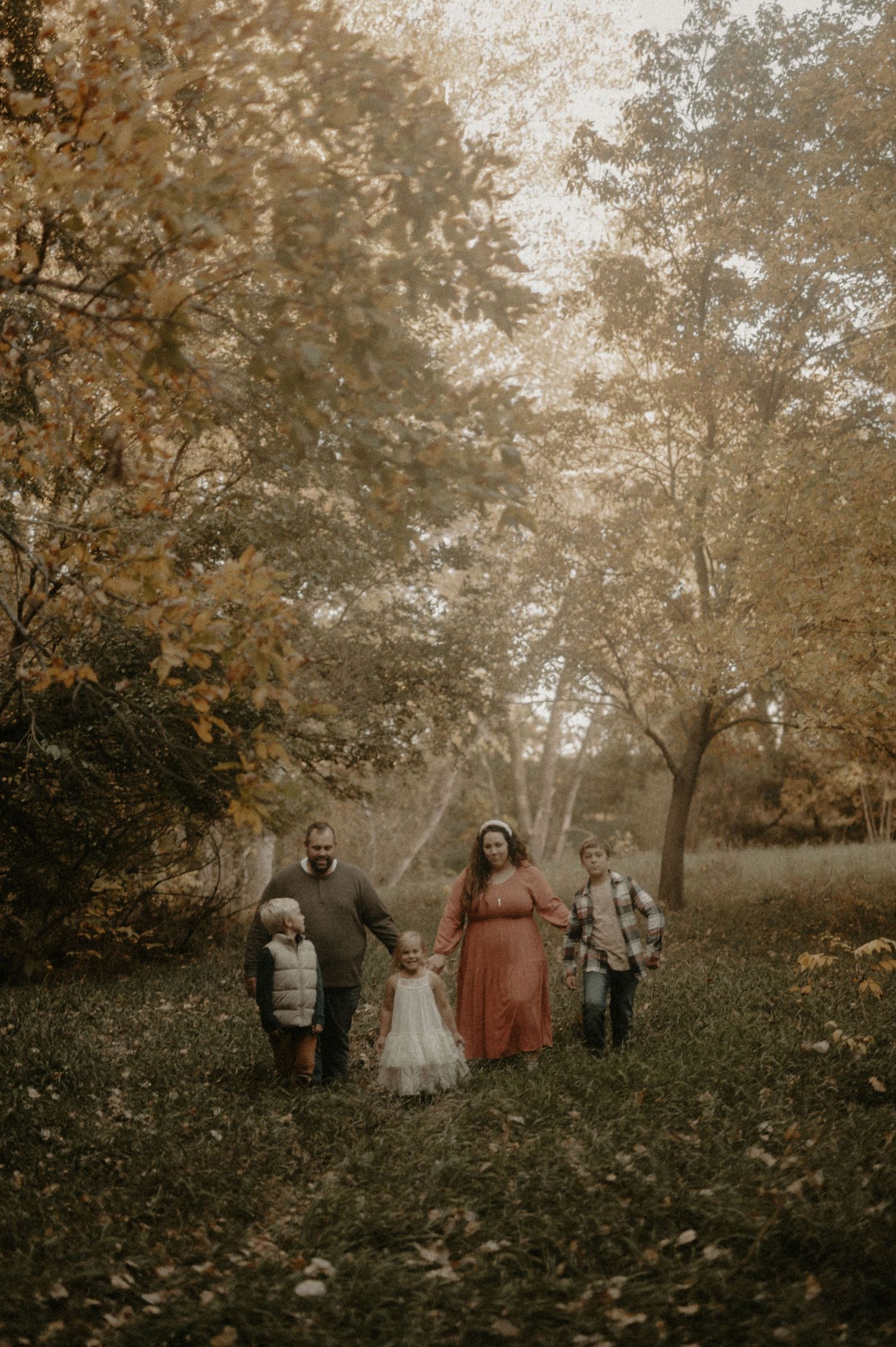 Family group walking together through a misty autumn forest with golden leaves.