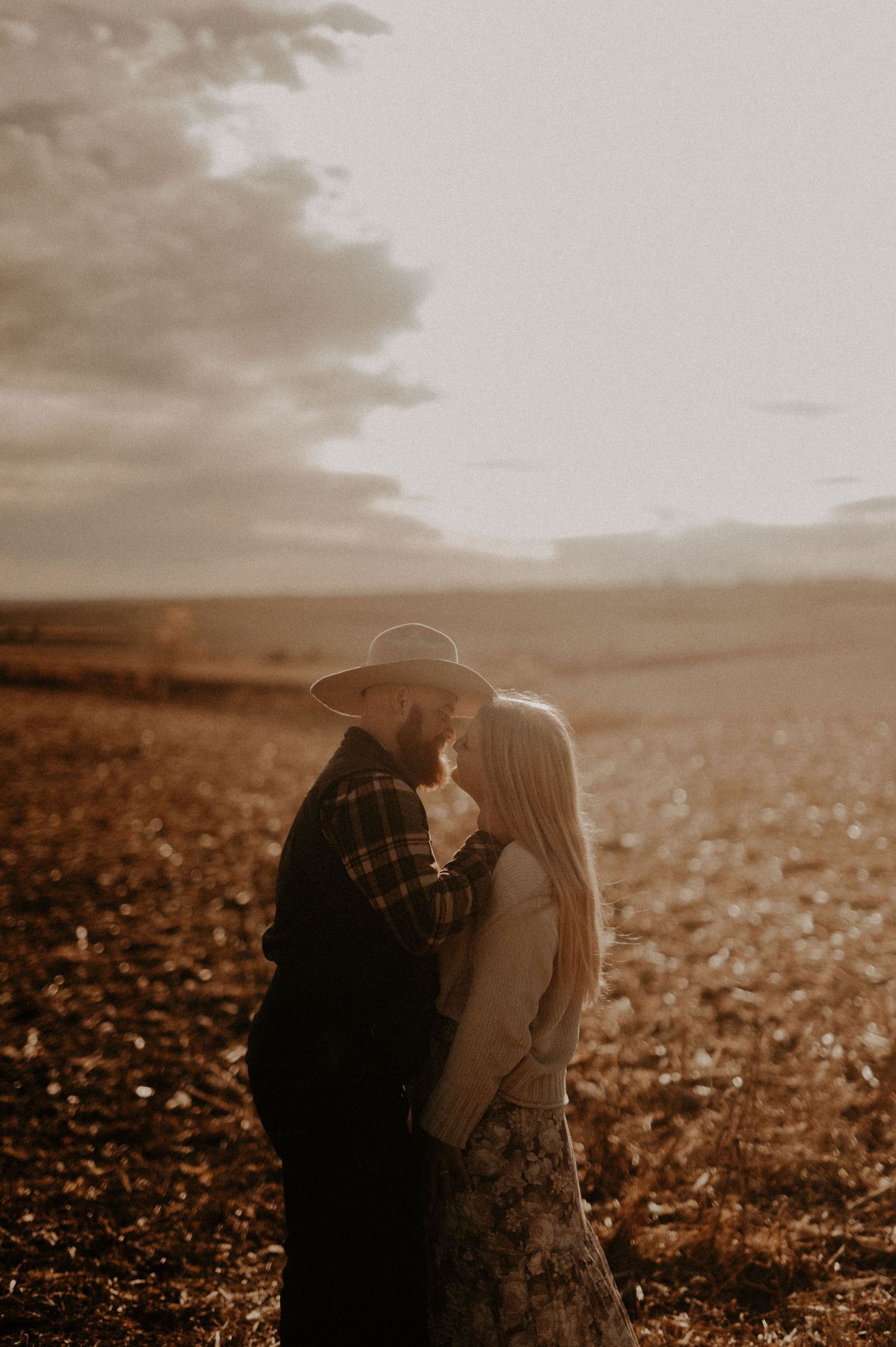 A romantic couple shares an intimate moment in a sunlit field at golden hour.