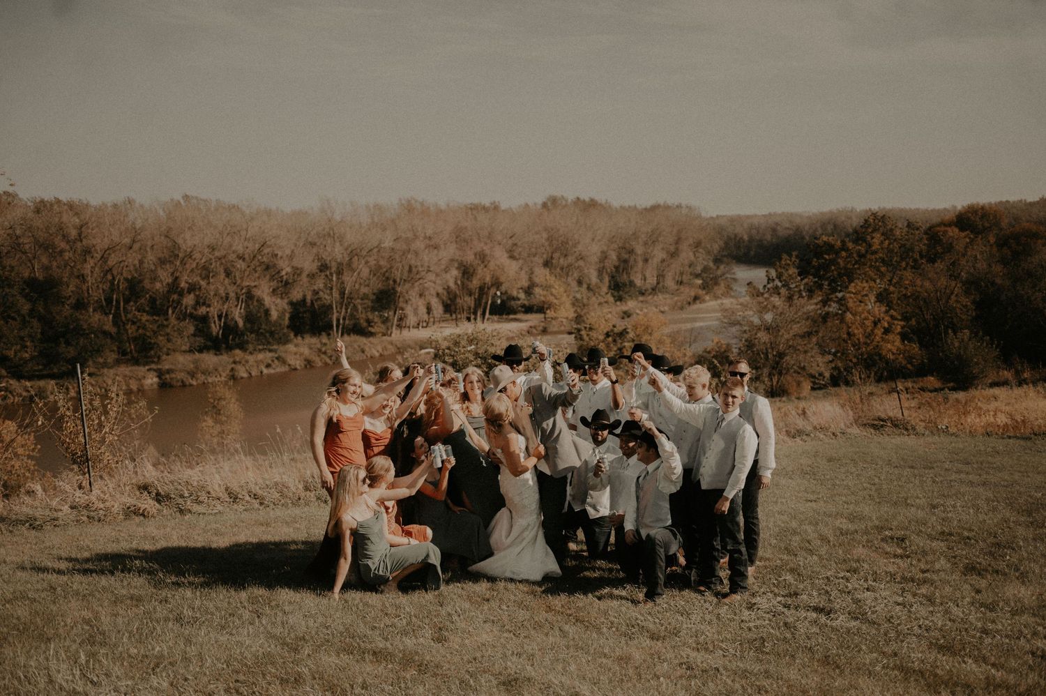Wedding party gathered in a field during golden hour with autumn trees in the background.